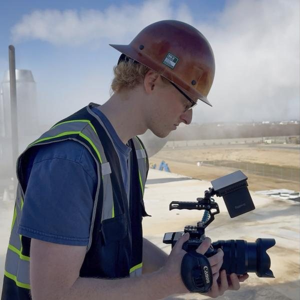 Grady Foster in a hard hat and safety vest, filming on a construction site.
