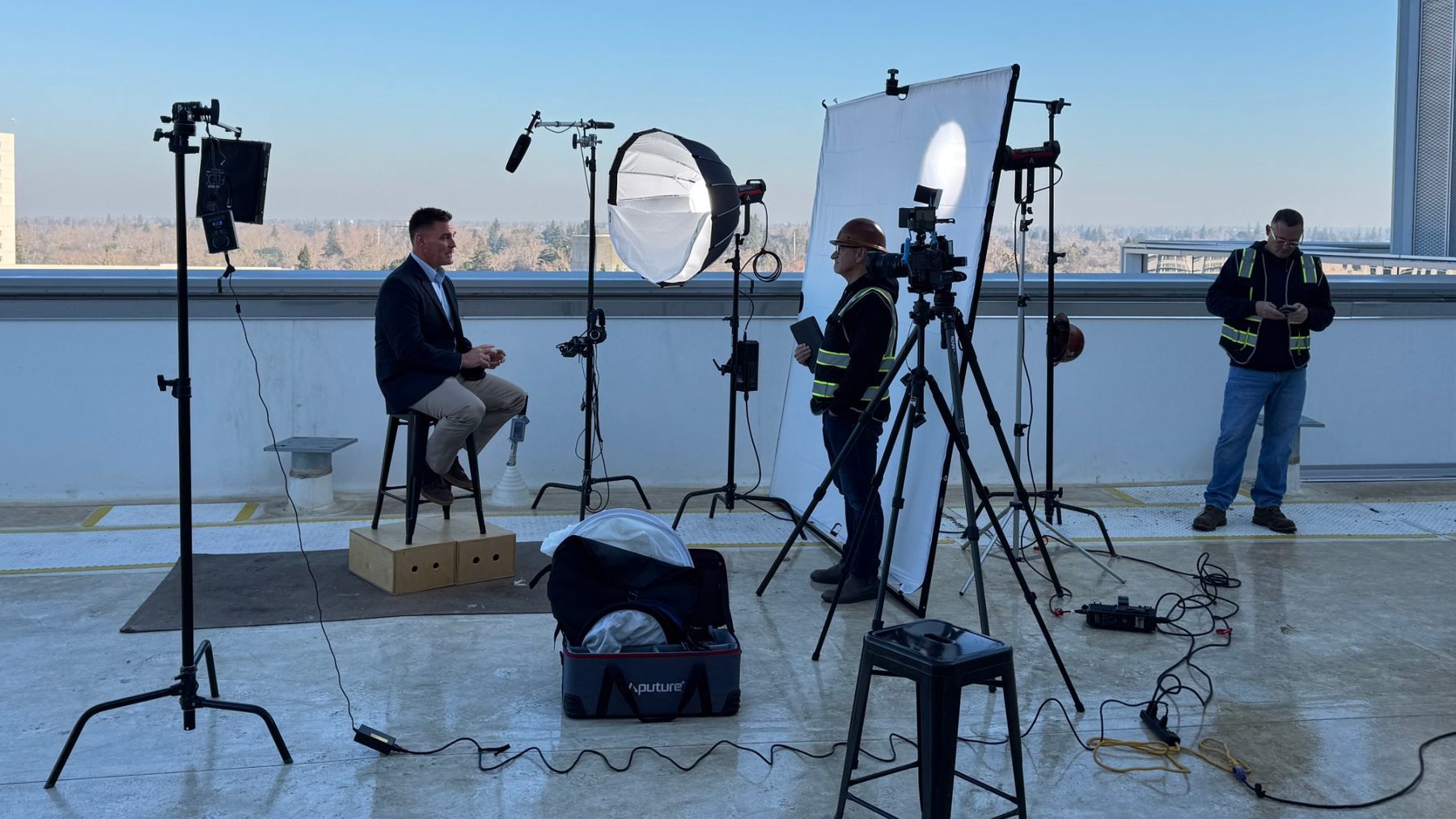 A Portlight interview set up on a Sacramento rooftop: the subject on a stool under a softbox, a camera operator in a hard hat and safety vest at the tripod.