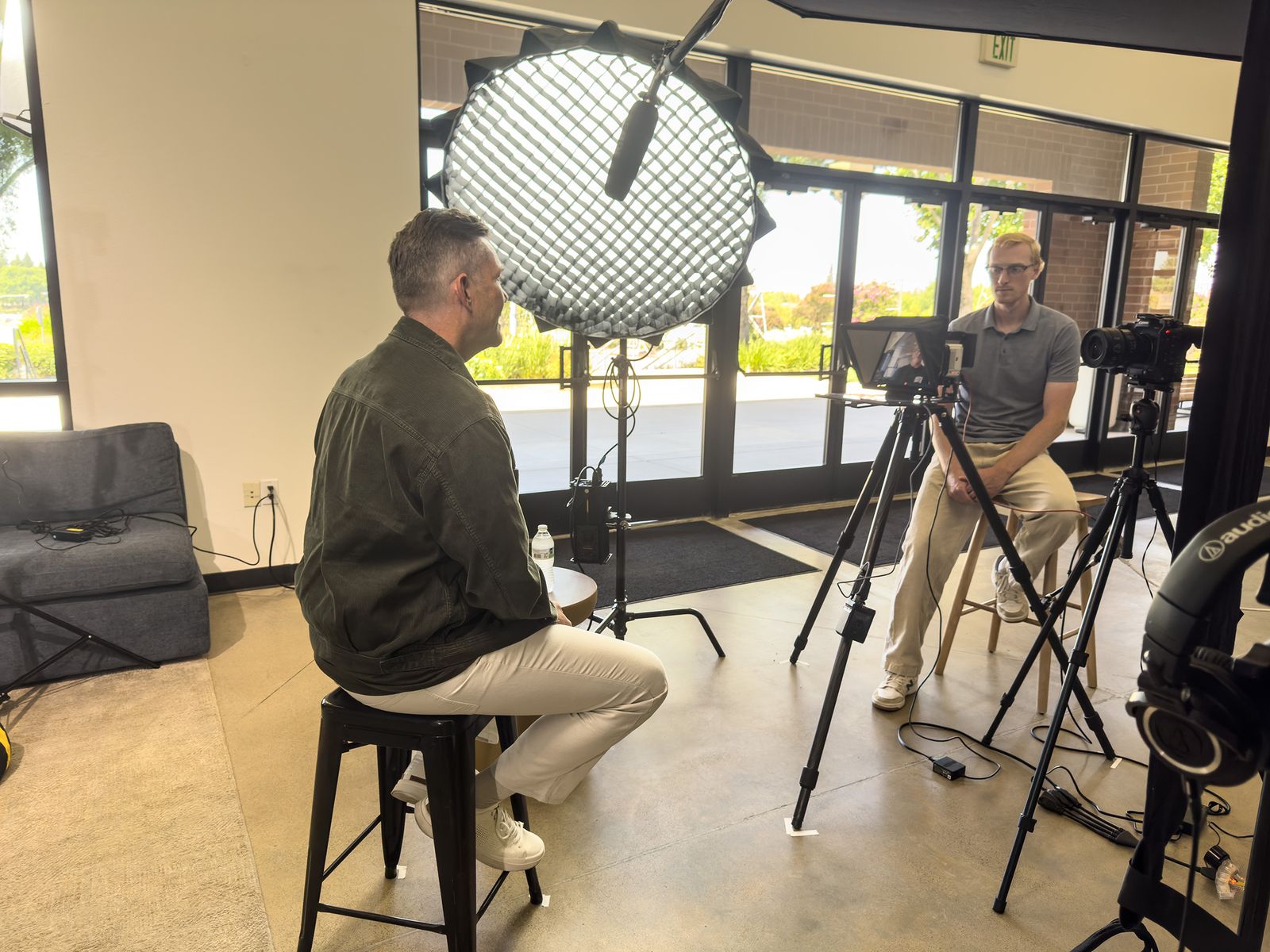 A Portlight interview in progress: the subject sits on a stool under a large softbox, facing the interviewer beside a teleprompter camera.